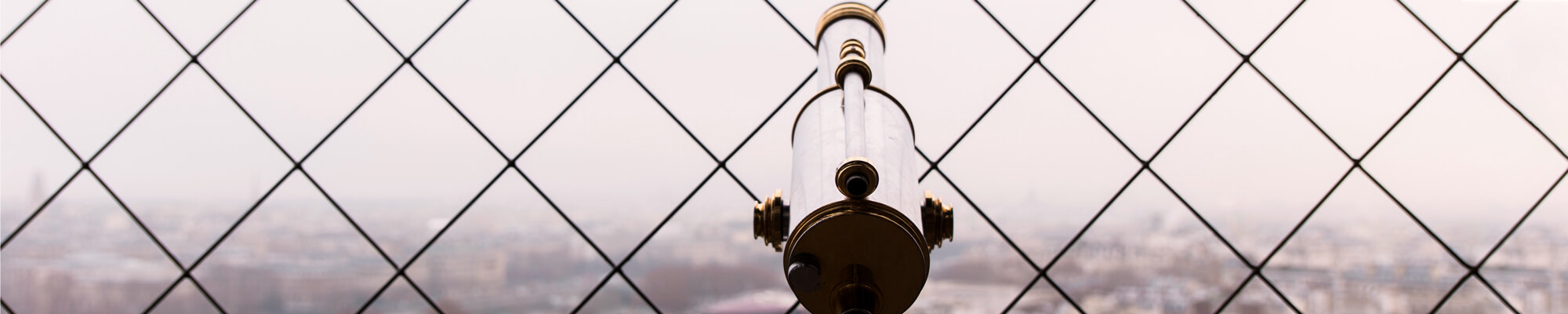 Abstract shot of a telescope in front of a fence with a cityscape in the background